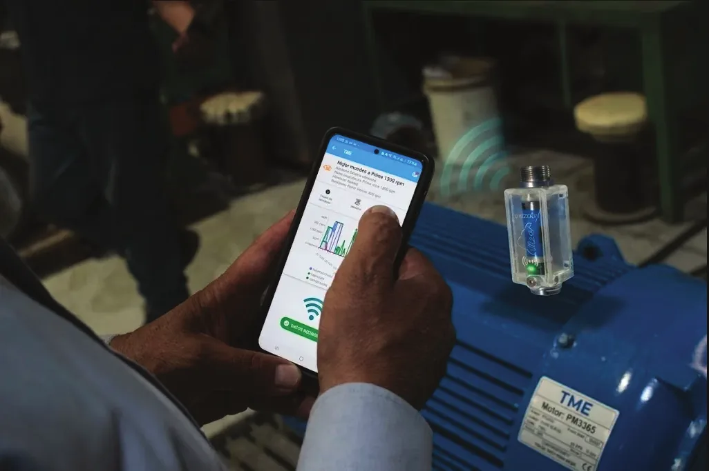 Técnico revisando en su celular el diagnóstico de un motor eléctrico con un sensor VIBZER colocado sobre la carcasa